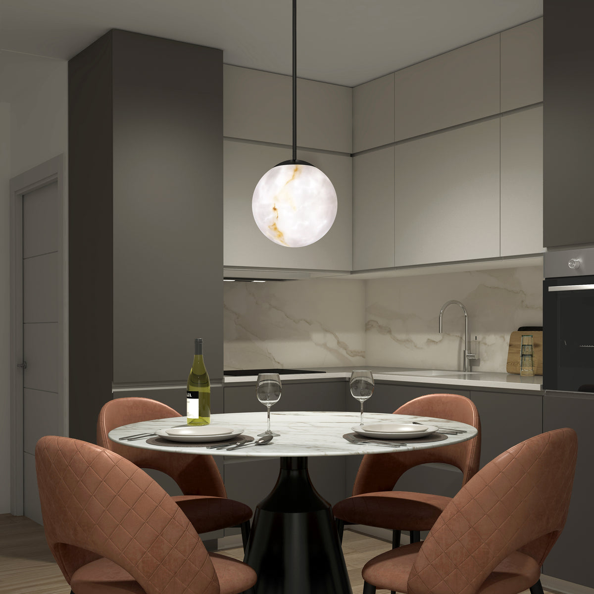 A modern kitchen with gray cabinets and a marble backsplash features a round table set for two, with wine glasses, a bottle of wine, and pink cushioned chairs under a spherical pendant light.