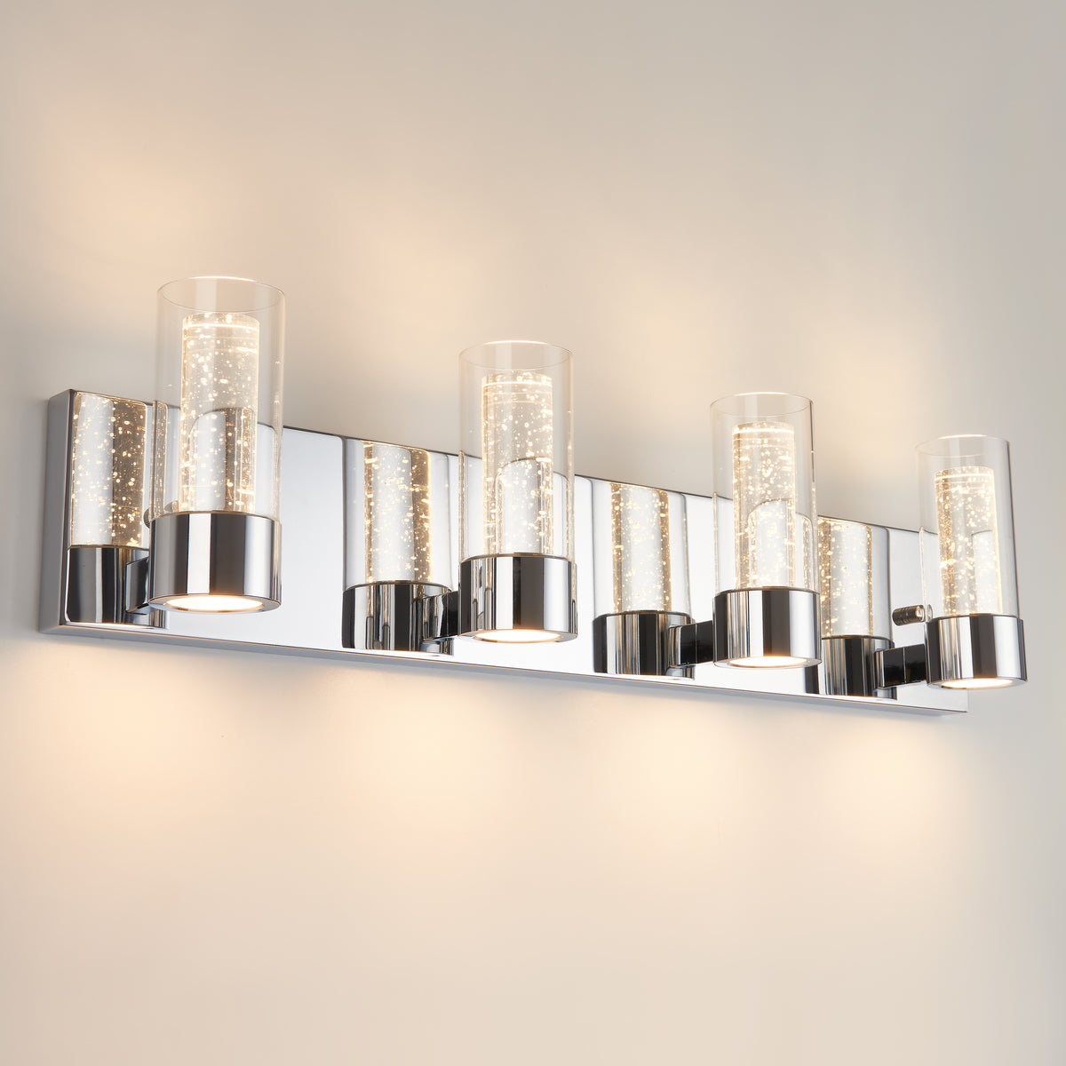 A modern wall-mounted light fixture with five cylindrical glass shades, each containing bubble details, set on a shiny chrome rectangular base. The fixture emits a soft, warm glow against a light-colored wall.