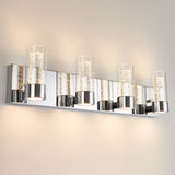 A modern wall-mounted light fixture with five cylindrical glass shades, each containing bubble details, set on a shiny chrome rectangular base. The fixture emits a soft, warm glow against a light-colored wall.