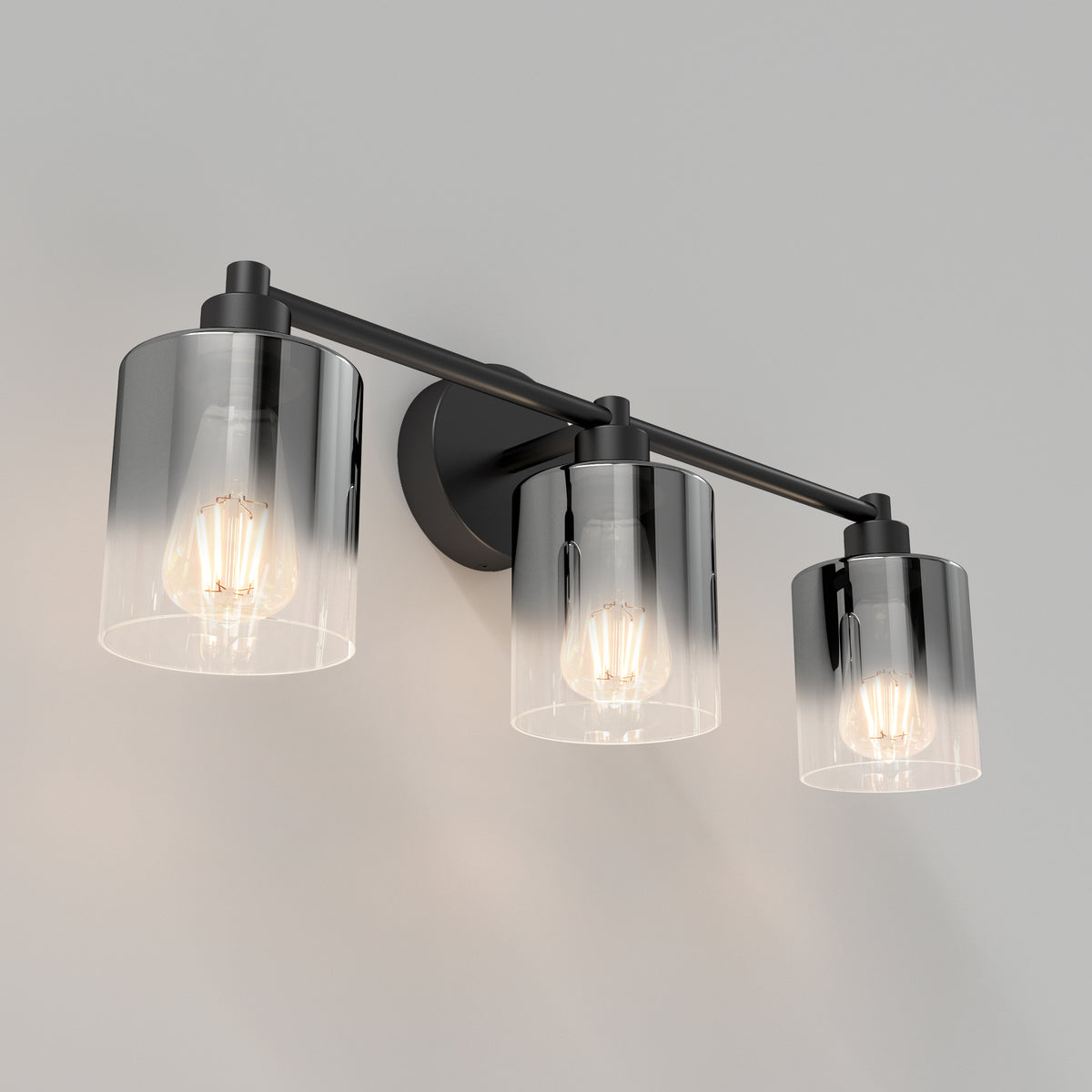A modern wall-mounted light fixture with three exposed bulbs, each encased in a cylindrical glass shade, attached to a black metal bar and circular base, against a plain light gray wall.