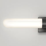 A modern wall-mounted light fixture with a frosted cylindrical glass shade and a rectangular black base, emitting a soft, even glow against a plain light-colored wall.