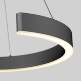 Close-up of a modern, circular hanging LED light fixture with a matte dark gray finish, suspended by thin wires against a plain light gray background.