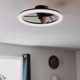 A modern ceiling fixture featuring a circular LED light with a small fan in the center, mounted on a white ceiling in a room with gray walls and a window with a dark curtain.