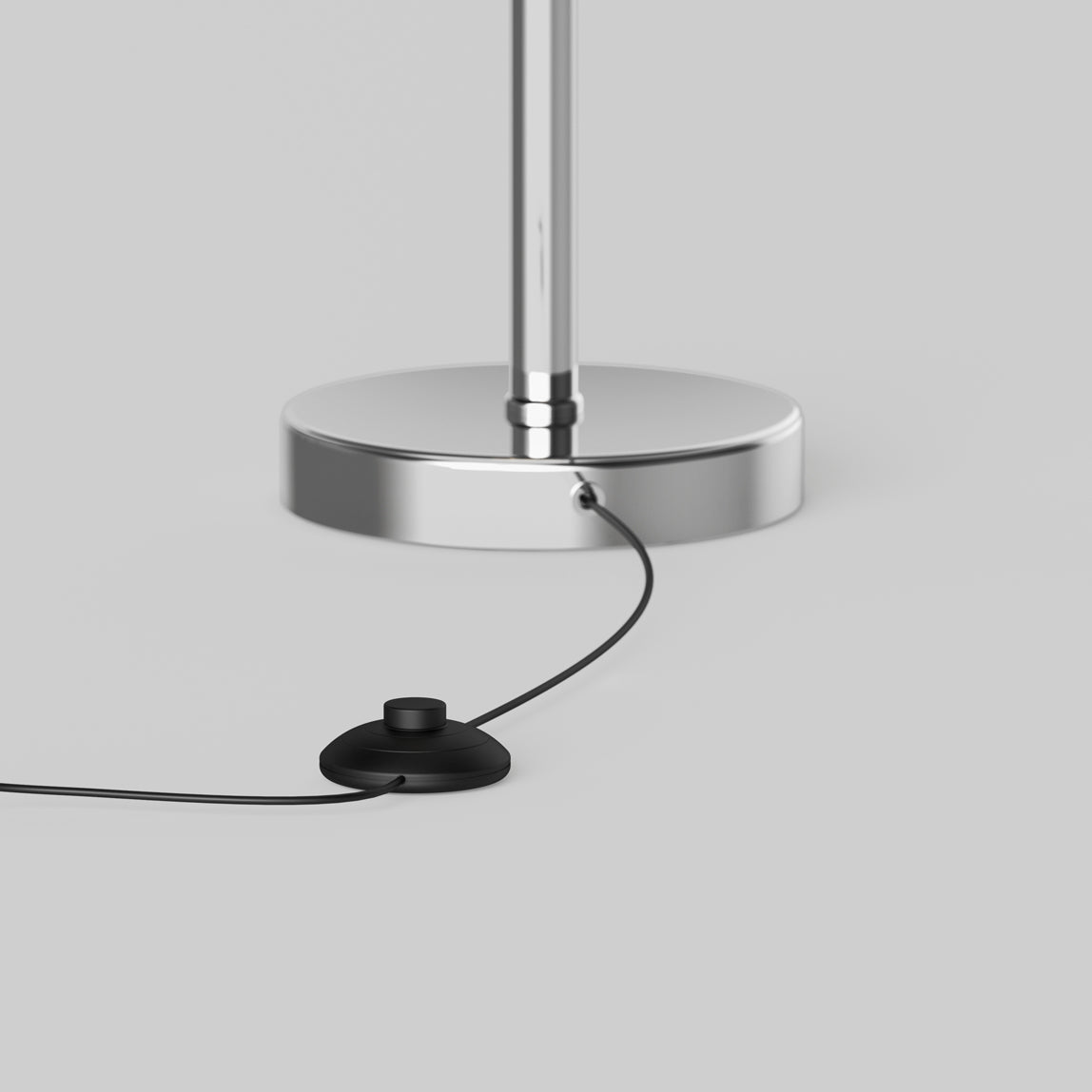 A close-up of the Artika Pivot modern LED floor lamp 3 CCT shows its chrome base with a connected black cord and round foot switch, displayed on a light gray surface.