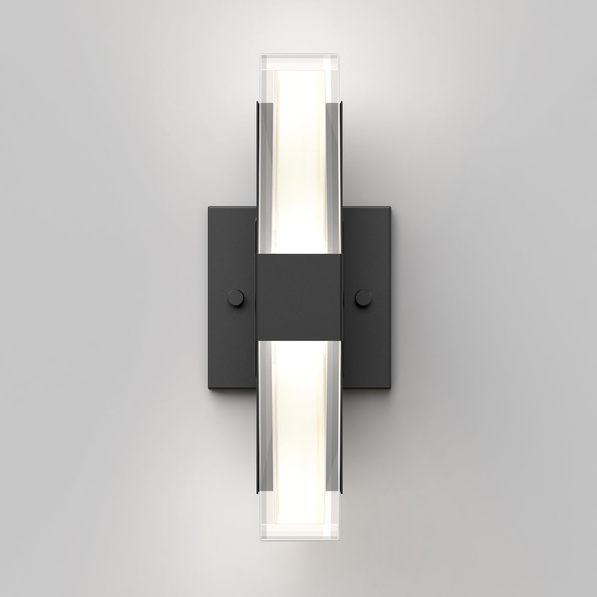 A modern wall sconce with a rectangular black base and two vertical light bars, emitting soft white light from the center. The design is minimalistic and geometric, mounted on a plain light gray wall.