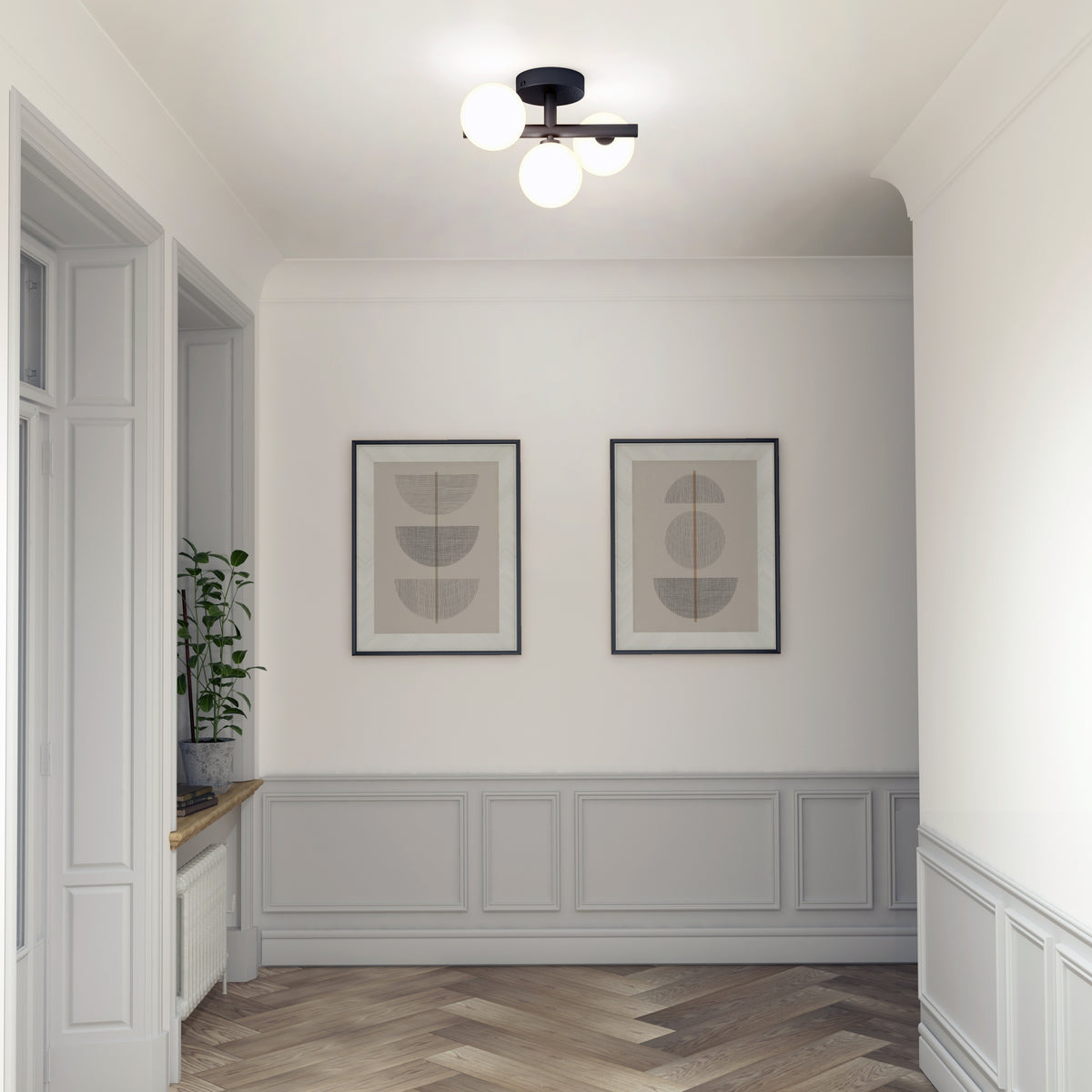 A minimalistic hallway features light gray paneling, two framed abstract art pieces on the wall, a potted plant on a windowsill, and a modern ceiling light with three round bulbs. The floor has a herringbone pattern.