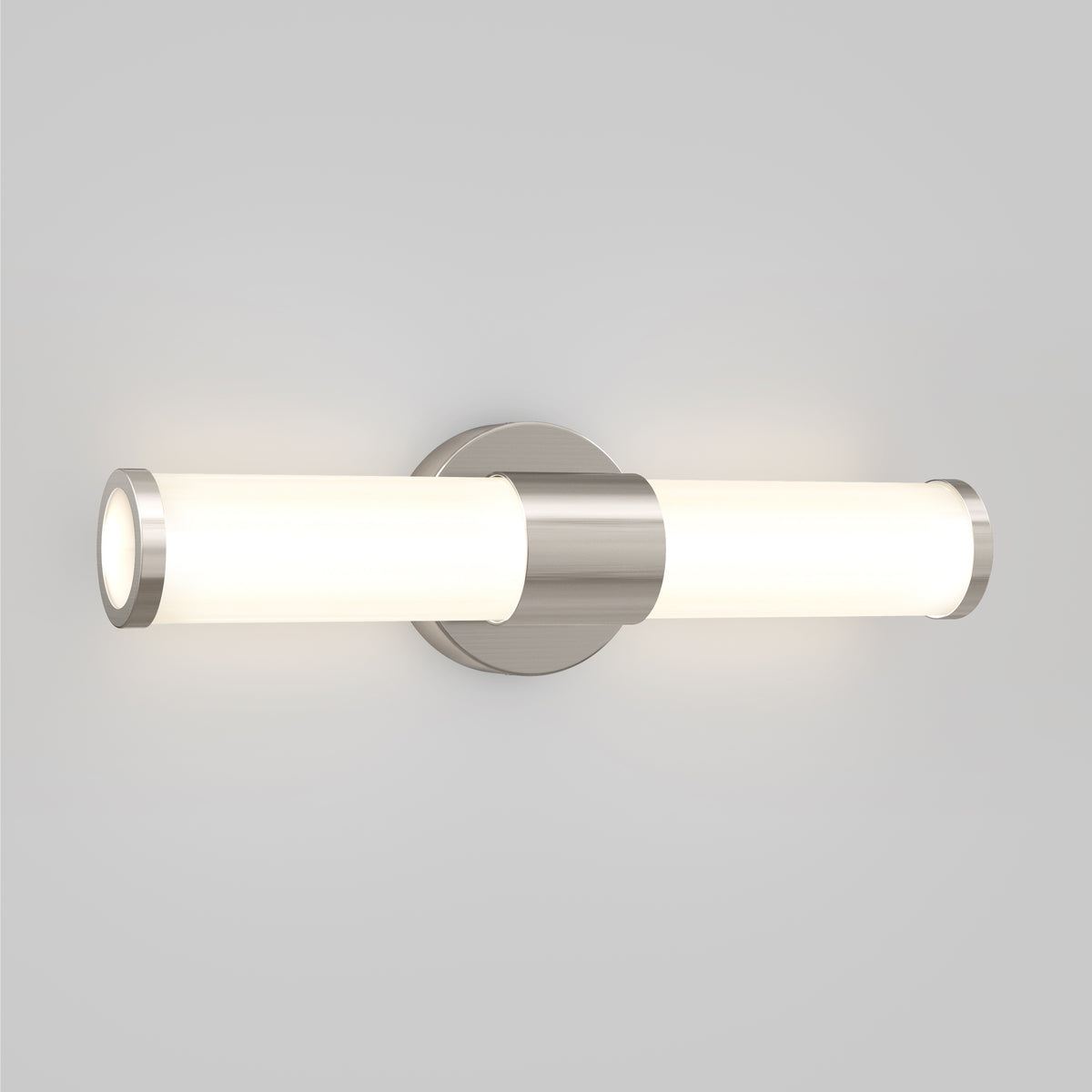 A modern wall-mounted light fixture with two cylindrical frosted glass shades and a brushed metal center, emitting soft white light, set against a plain light gray background.