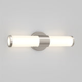 A modern wall-mounted light fixture with two cylindrical frosted glass shades and a brushed metal center, emitting soft white light, set against a plain light gray background.