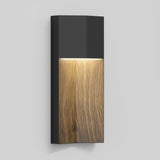 A modern wall sconce with a matte black top and a wood-grain finish on the lower half, emitting a soft light downward against a plain light gray background.