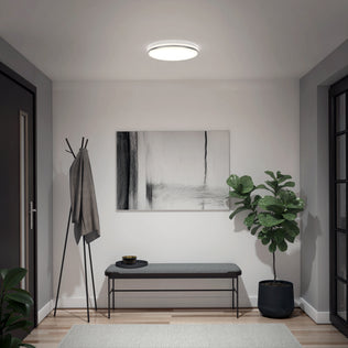 A modern hallway with a bench, coat rack, plant, and art under the Artika Macy 15 in. LED RGB Wifi smart ceiling light.