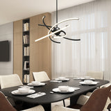 A modern dining room with a black table set for six, cream upholstered chairs, a unique abstract chandelier, floor-to-ceiling windows with sheer curtains, and built-in wooden bookshelves in the background.