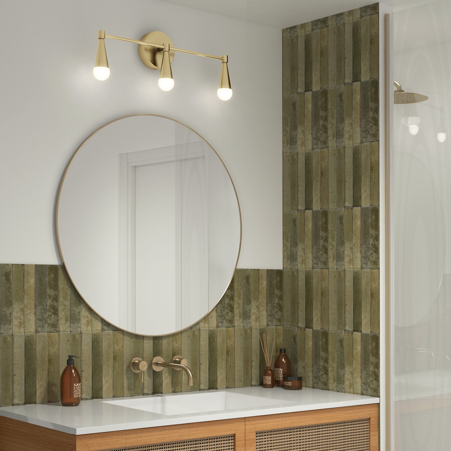 A modern bathroom features a round mirror above a wooden vanity, brass faucet, and the Artika Wayden LED mid-century bathroom vanity light (3 CCT). Olive green vertical tiles line the wall, with toiletries neatly arranged on the sink counter.