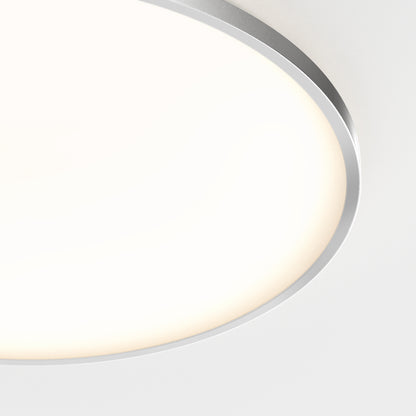 A close-up of the Artika Europa 21 in. LED modern flush mount light, featuring a white diffuser and metallic rim, emits a soft glow on a white ceiling. Includes remote control for adjustable lighting.