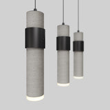Three modern cylindrical pendant lights with a gray concrete texture and black metal bands hang from the ceiling against a plain light gray background. The lights are illuminated at the bottom.