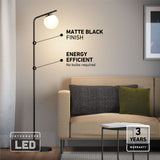 A modern floor lamp with a matte black finish stands next to a beige sofa with cushions. Text highlights its energy efficiency, integrated LED, and 3-year warranty. A small table and wall art are also visible.