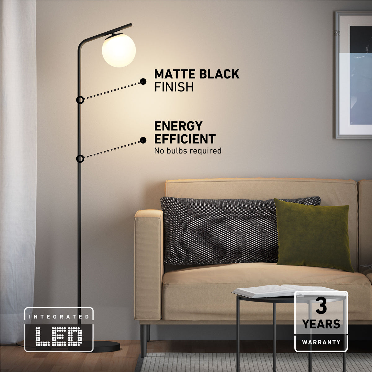 The Artika Clayton dimmable LED modern mid-century floor lamp, with a matte black finish and energy-efficient round LED light, stands by a beige sofa with dark and green cushions. Includes a “3 Years Warranty” label.