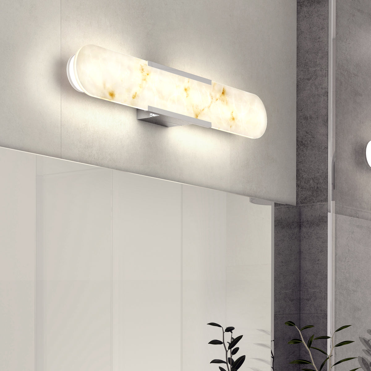 A modern, oval-shaped wall sconce with a frosted, marbled white glass cover emits a warm light. The fixture is mounted above a large mirror on a light gray bathroom wall. Some green plant leaves are visible below.