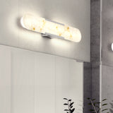 A modern, oval-shaped wall sconce with a frosted, marbled white glass cover emits a warm light. The fixture is mounted above a large mirror on a light gray bathroom wall. Some green plant leaves are visible below.
