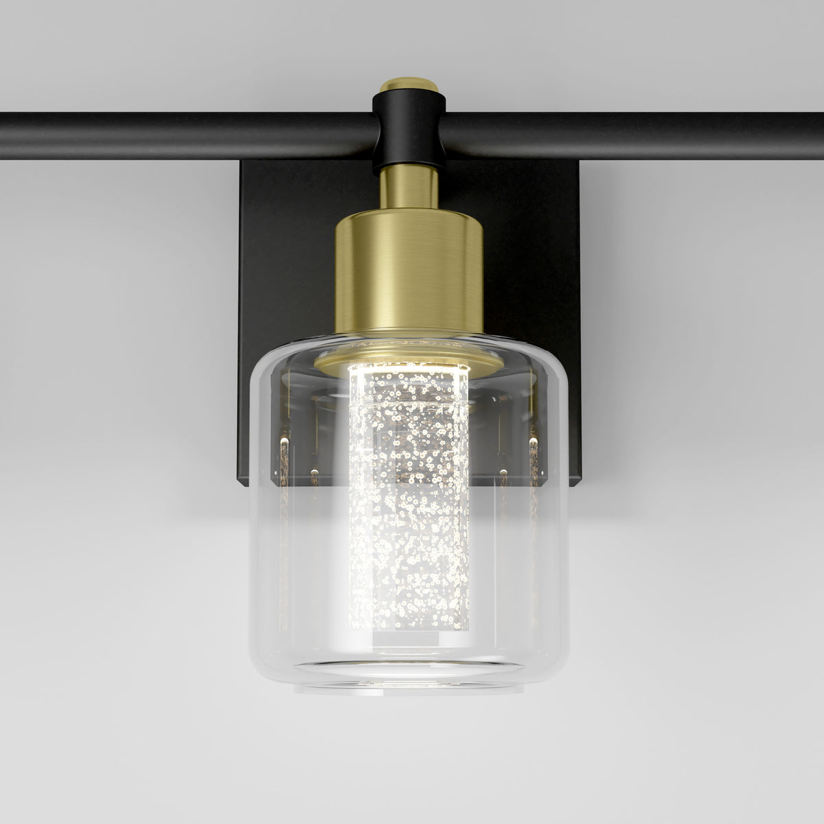 A modern wall sconce with a cylindrical glass shade, a gold metal top, and a textured inner light fixture, mounted on a black rectangular backplate against a white wall.