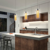 Modern kitchen with wood cabinets, a large island with a sink, gray countertop, and three hanging pendant lights. There are two black chairs by the island and a spiral staircase in the background. Fruit sits on the counter.