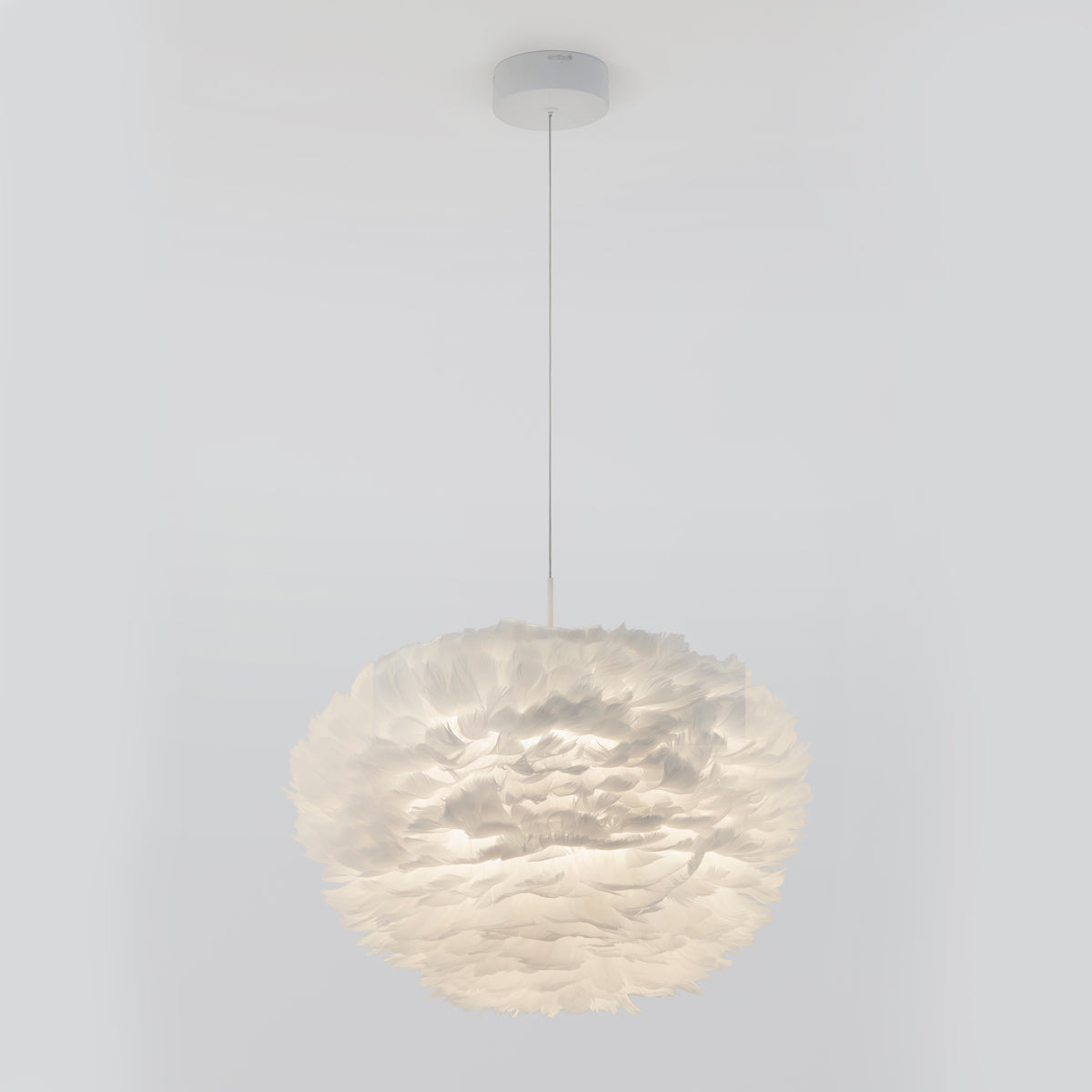 The Artika Plume LED pendant light features a spherical shade crafted from layered, feather-like white material and hangs elegantly from the ceiling by a thin cord against a plain white background.