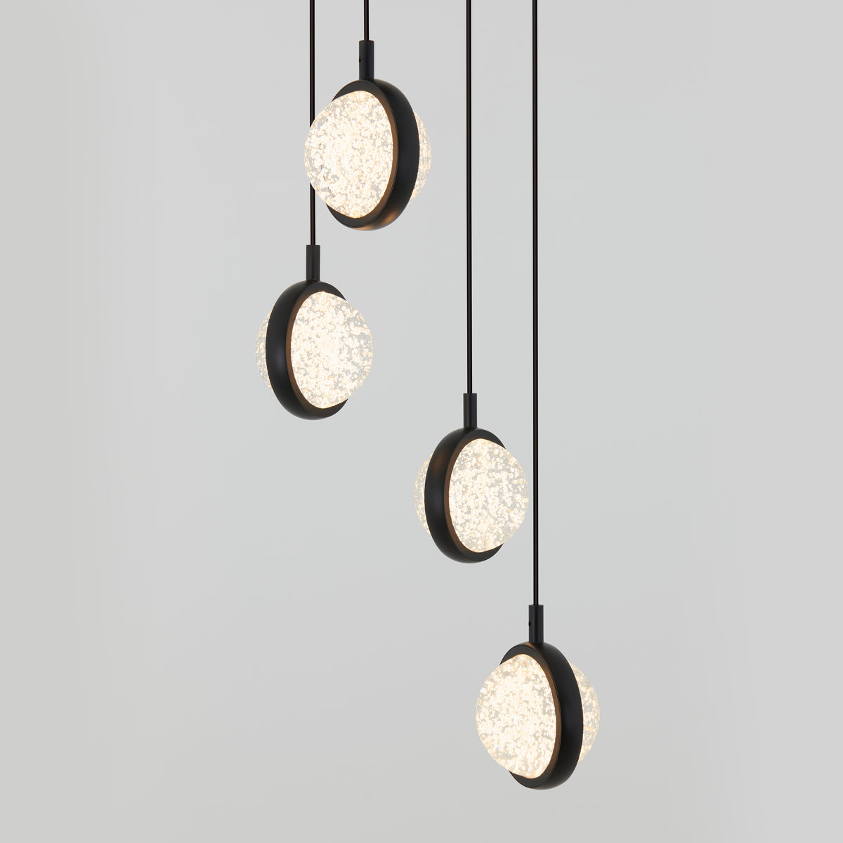Four modern pendant lights with round, textured glass shades and black frames hang at different heights against a plain light gray background.