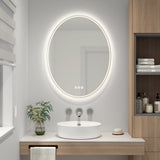 A modern bathroom features a round, illuminated mirror above a white vessel sink on a wooden vanity. A small plant, soap dish, and neatly folded towels complete the clean, minimalist decor.