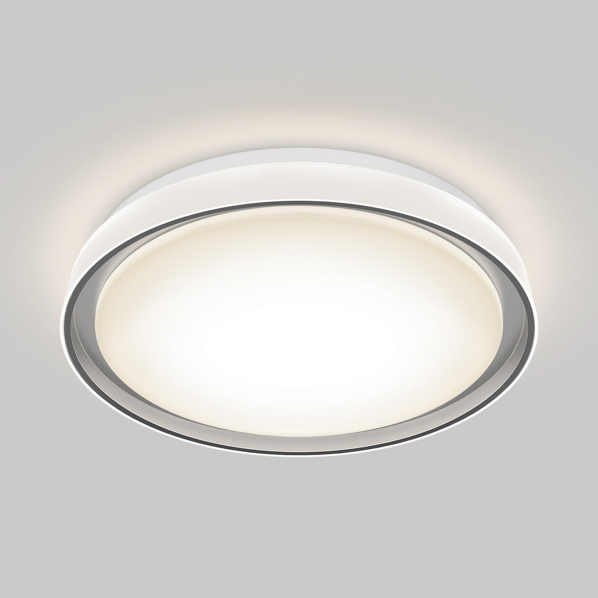 A modern, round ceiling light fixture with a white frosted cover and metallic trim, mounted on a light gray ceiling, emitting a bright, even glow.