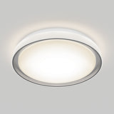 A modern, round ceiling light fixture with a white frosted cover and metallic trim, mounted on a light gray ceiling, emitting a bright, even glow.