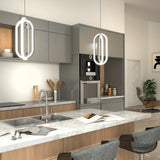 A modern kitchen with gray and wood cabinets, marble countertop, built-in appliances, two pendant lights, a sink, and bar stools. There are jars and utensils on the counter, and a stylish lounge chair in the background.
