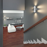 A modern interior with a gray staircase leading to a living room featuring white furniture, a round glass coffee table, built-in shelves, a TV, wooden floors, and sleek wall-mounted lights.
