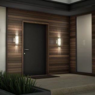 A modern house entrance features a dark door, wood paneling, Artika Bubble Element LED indoor-outdoor lights on either side, a welcome mat, frosted glass window, and a small planter with green plants.