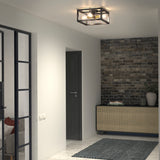 A modern hallway with a black-framed ceiling light, a console table with books and a plant, a textured brick accent wall, a dark door, and a glass-paneled wall revealing part of a sofa and cushions.