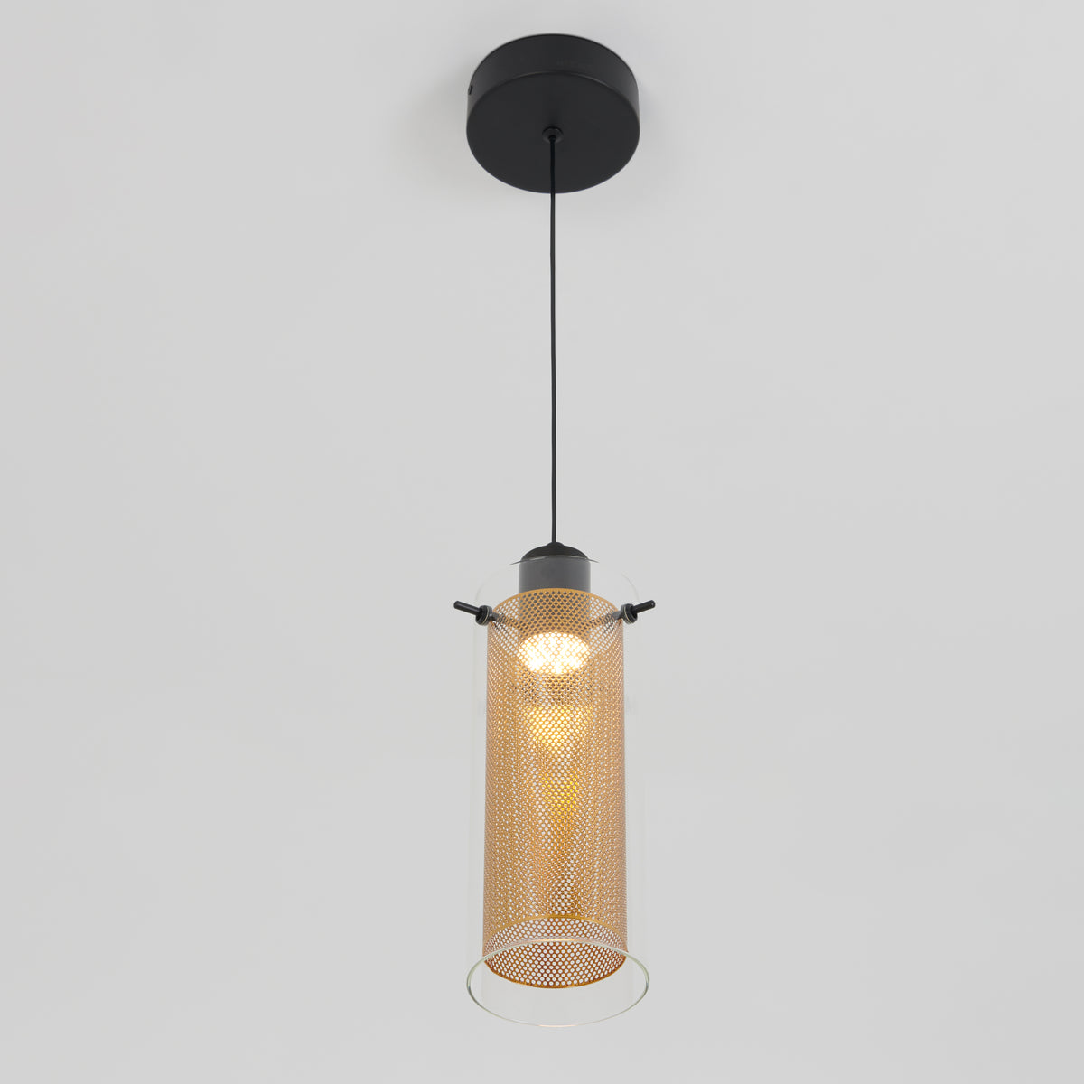 The Artika Oxion 1-light LED pendant features a black ceiling mount and a cylindrical, perforated gold metal shade suspended from a black cord, casting soft light against a white background.