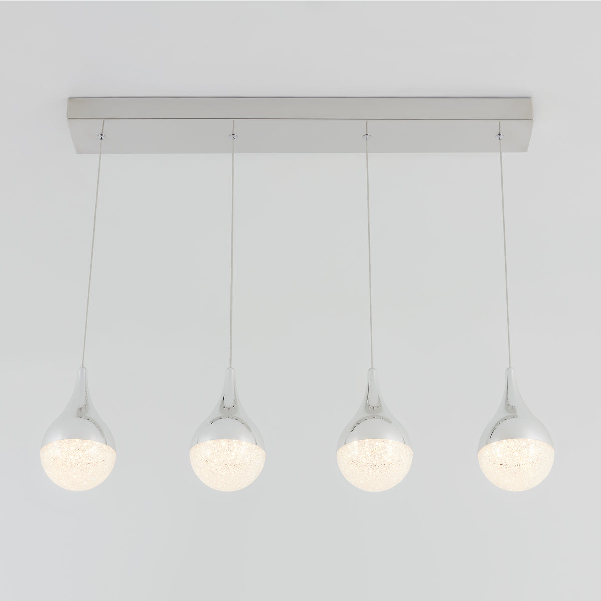 A modern ceiling light fixture with four teardrop-shaped, chrome-finished pendant lights hanging in a row from a rectangular base against a white background.