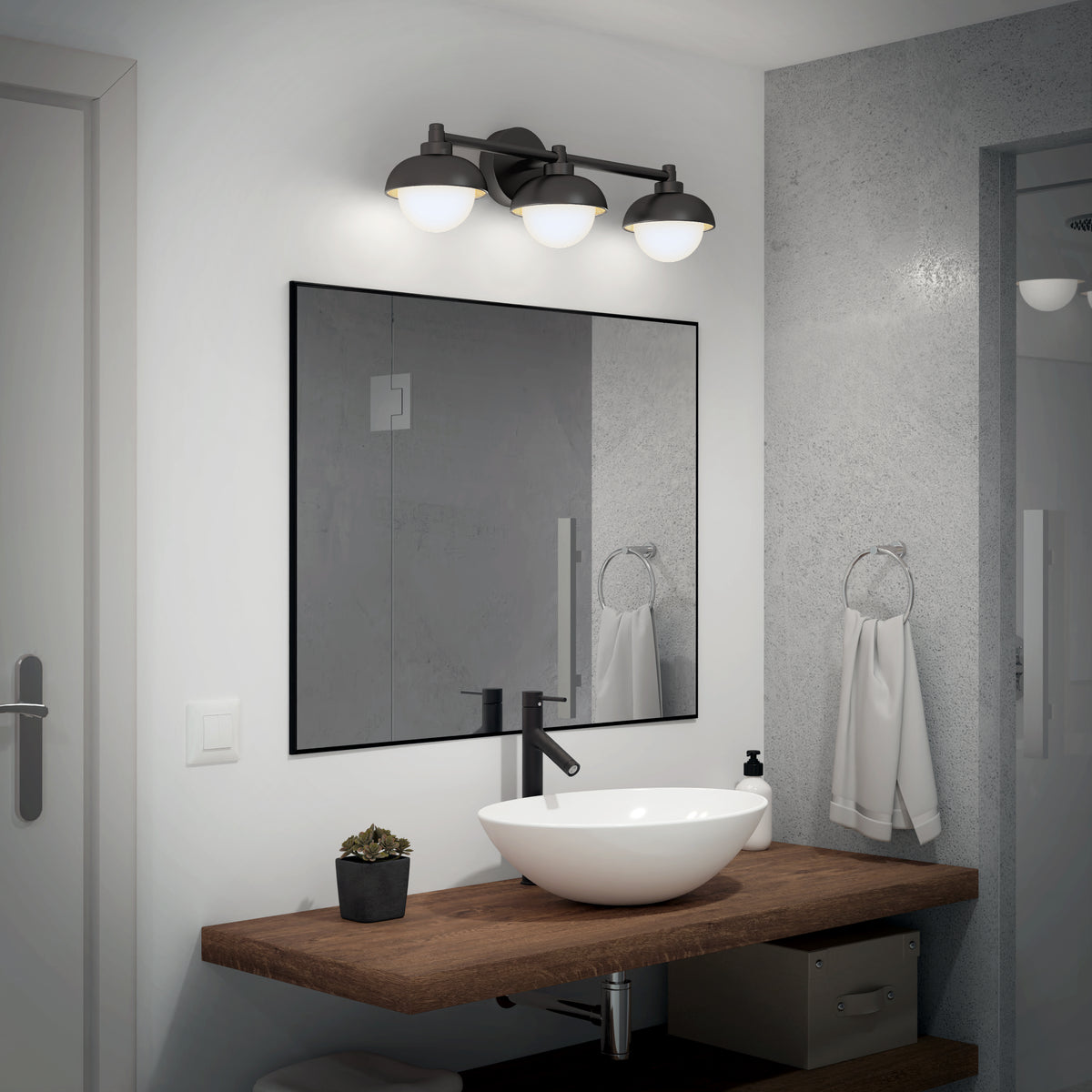 A modern bathroom featuring a wall-mounted wooden vanity, white vessel sink, black faucet, round mirror, Artika Boden 27-in Integrated LED 5-CCT Vanity Light Bar, towel ring with white towel, soap dispenser, and a small potted plant.
