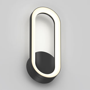 The Artika Aiden modern LED indoor-outdoor wall light 5 CCT features a black circular base and an oval LED frame, mounted vertically on a plain light gray wall.