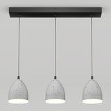 Three modern pendant lights with gray, speckled, dome-shaped shades hang in a row from a rectangular black ceiling mount against a plain white background. The lights are evenly spaced and turned on.