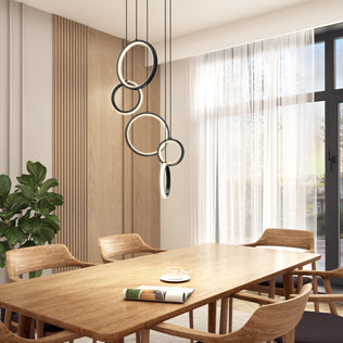 A modern dining room features a wooden table with chairs, a green potted plant, sheer-curtained window, and the Artika Elmo 5-light LED pendant above. The table is set with plates and a cup.