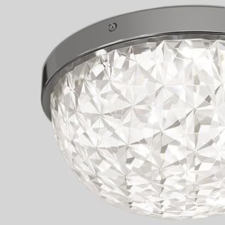 Close-up of the Artika Carat LED flush mount light, featuring a faceted dome-shaped glass cover and shiny metallic rim, creating a geometric, sparkling look against a plain gray background.