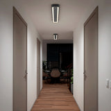 A modern hallway with wooden floors, white walls, two closed doors on each side, and ceiling lights. At the end of the hallway is a dining area with chairs, a table, and large windows.