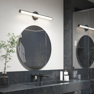 Modern bathroom with Artika Ewen LED vanity light above a round mirror, dark marble countertop, and small potted plant.