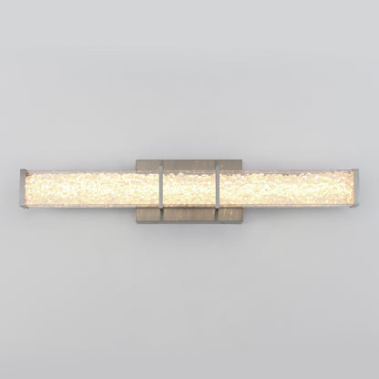 A modern wall-mounted light fixture with a rectangular frosted glass shade and metallic accents, emitting a soft, warm glow against a plain light gray background.