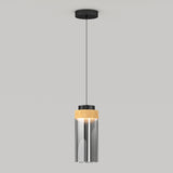 A modern pendant light with a black ceiling mount, a thin black cord, and a cylindrical glass shade featuring a wooden accent near the top, hanging against a plain gray background.