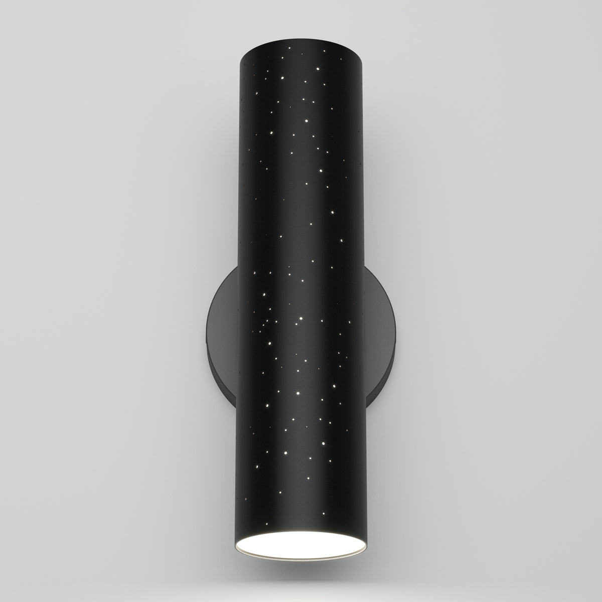 A modern black cylindrical wall sconce with small star-like holes and a glowing white light at the bottom, mounted on a plain light gray wall.