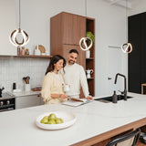 A smiling couple stands together in a modern kitchen, looking at a cookbook on the counter. The kitchen features pendant lights, wooden cabinets, and a bowl of green apples on a white island.