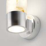 A modern wall sconce with a cylindrical frosted glass shade and a shiny chrome base, mounted on a round wall plate, emitting soft white light against a neutral wall.