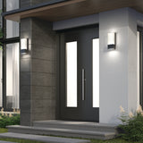 Modern front entrance with a black door featuring vertical frosted glass panels, two wall-mounted rectangular lights on either side, concrete steps, and minimal landscaping.