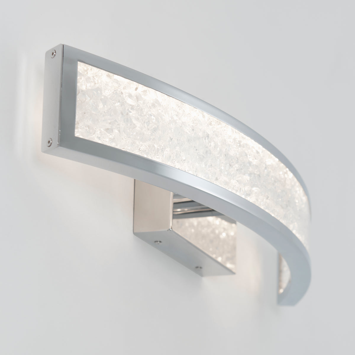 A modern wall-mounted light fixture with a curved, silver frame and a textured, frosted glass panel emitting bright, white light against a plain white wall.
