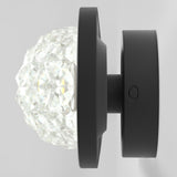 A modern wall-mounted light fixture with a faceted glass globe and a matte black circular base, shown against a plain light gray background.